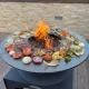 Brasero plancha Fiesta 75 cm en acier corten avec feu central et légumes grillés en situation d'utilisation