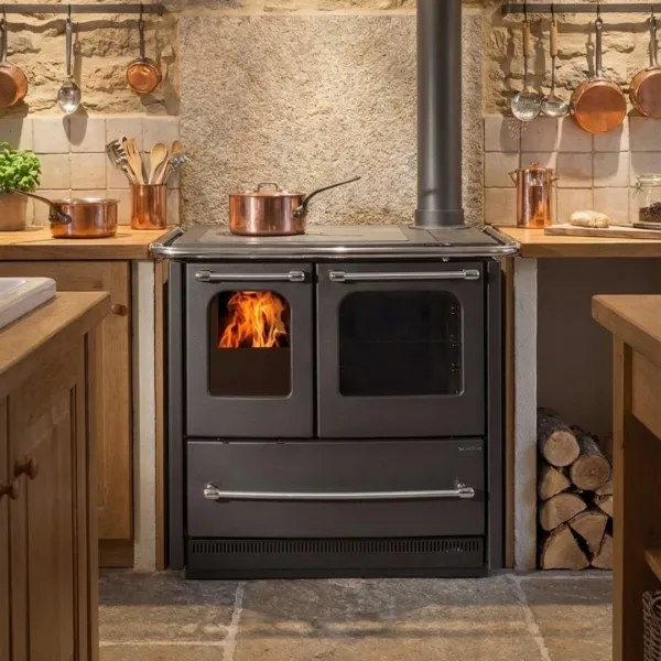 Cuisinière à bois SOVRANA EASY EVO noire avec four intégrée dans cuisine rustique avec feu allumé