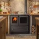 Cuisinière à bois SOVRANA EASY EVO noire avec four intégrée dans cuisine rustique avec feu allumé