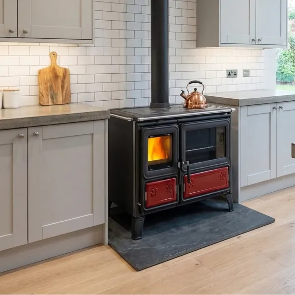Cuisinière à bois Milly noire et rouge avec four, installée dans une cuisine moderne avec feu allumé