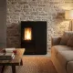Poêle à granulés Sharon Plus steel noir 10 kW allumé dans un salon avec mur en pierre apparente