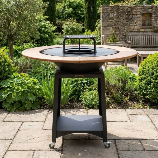 Brasero plancha Kit Fiesta Ø75 cm avec table ronde en bois installé dans un jardin