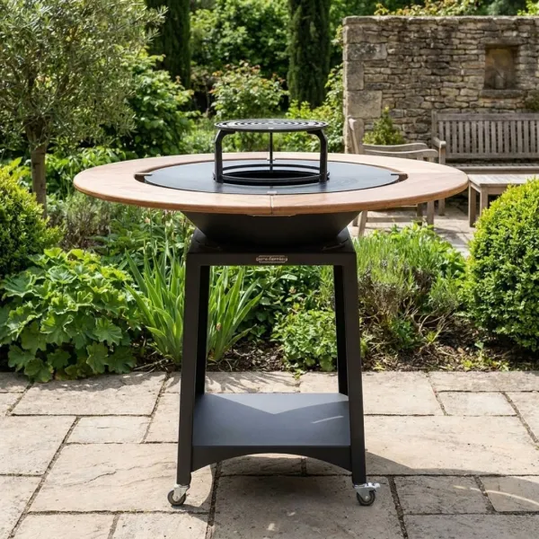 Brasero plancha Kit Fiesta Ø75 cm avec table ronde en bois installé dans un jardin