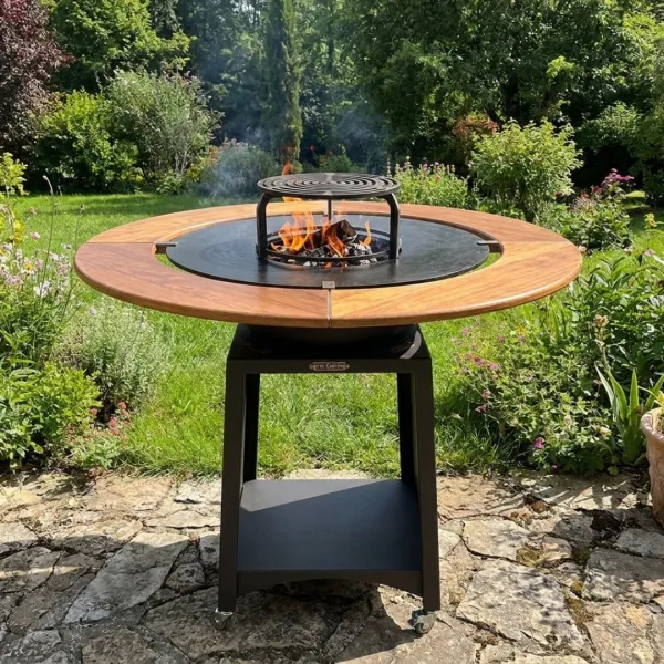 Brasero plancha Kit Fiesta Ø75 cm avec table en bois et feu apparent dans un jardin
